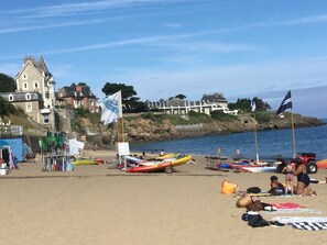 A beach with kayaks, a flag, and a building in the background. - DINARD VACATION RENTAL HOUSE (Dinard)