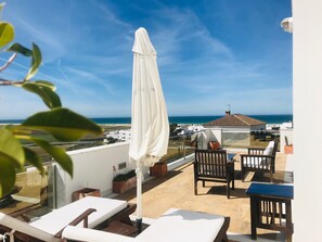 Une terrasse sur le toit avec vue sur la mer, un parasol blanc et du mobilier d’extérieur.