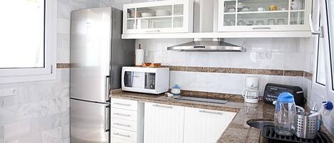 A modern kitchen with white cabinetry, a stainless steel refrigerator, a microwave, and a coffee maker.