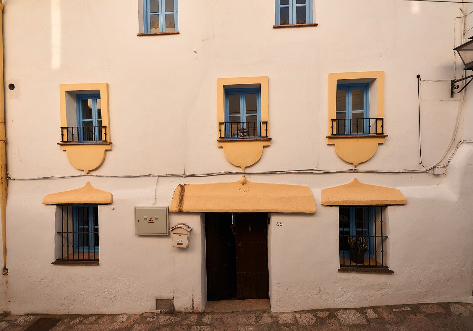 Ein Gebäude mit drei Fenstern, jedes mit einem Balkon. Eine Tür trägt die Nummer 66.