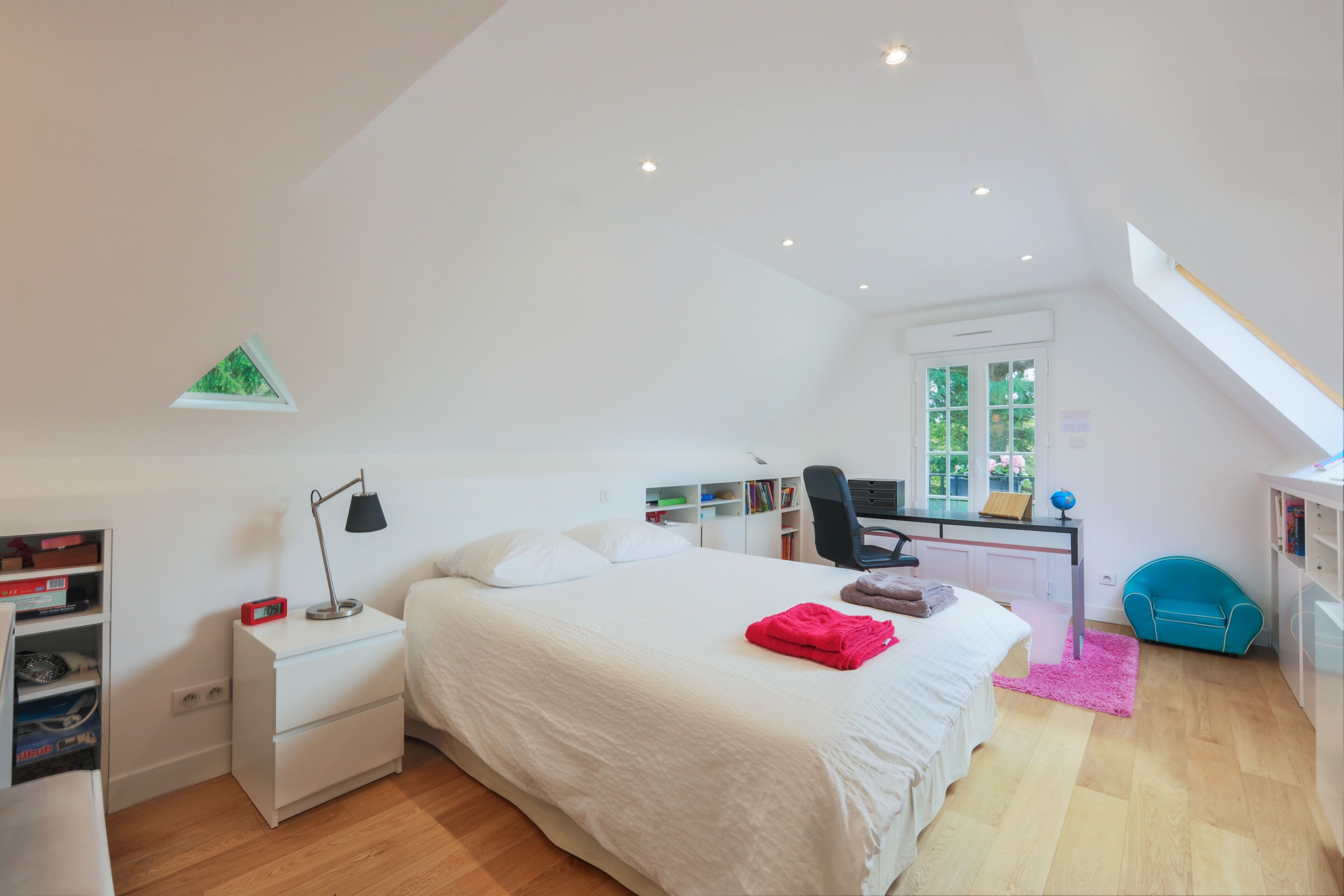 A bedroom with a bed, bedside table, desk, chair, and a window.