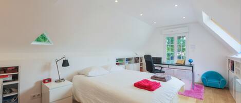A bedroom with a bed, bedside table, desk, chair, and a window.