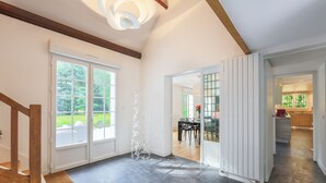 Una habitación amplia con una escalera, un comedor y una cocina visibles a través de puertas de cristal.