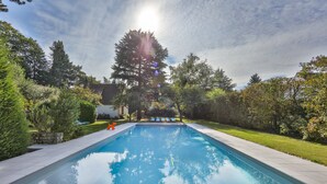 Una piscina rectangular con superficie de agua azul cristalina, rodeada por un suelo empedrado y abundante vegetación.