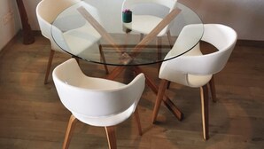 A round glass table with six white chairs, wooden legs, and a small green object on the table.