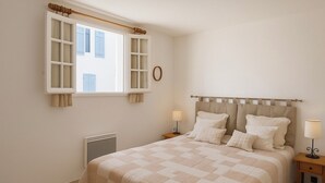 Une chambre à coucher avec un lit, deux tables de chevet, un radiateur et une fenêtre avec des rideaux.