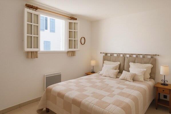 A bedroom with a bed, two bedside tables, a radiator, and a window with curtains.