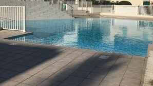 Une piscine dont le sol est recouvert de carrelage, avec des rampes blanches et, en arrière-plan, des bâtiments dont les toits sont également recouverts de tuiles.