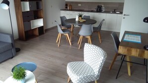 Un soggiorno moderno con angolo pranzo, una cucina con mobili bianchi e una libreria in legno.