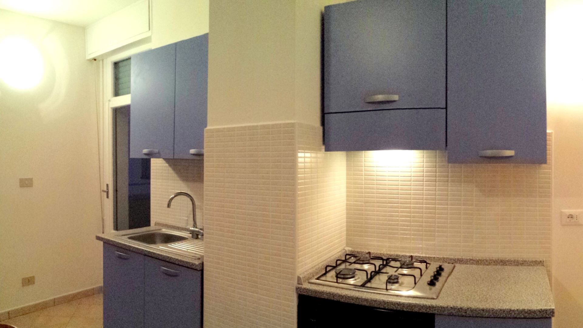 A compact kitchen with a gas stove, a sink, and blue cabinets.