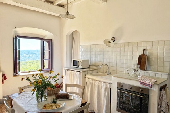 A kitchen with a view, a dining table with a vase of flowers, a microwave, and a sink.