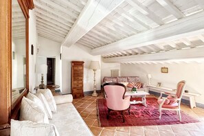 A spacious room with a high ceiling, a large mirror, a sofa, two chairs, a table, and a fireplace.