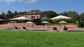 Ein Gebäude aus Stein mit Poolbereich, Sitzgelegenheiten im Freien und Sonnenschirmen.