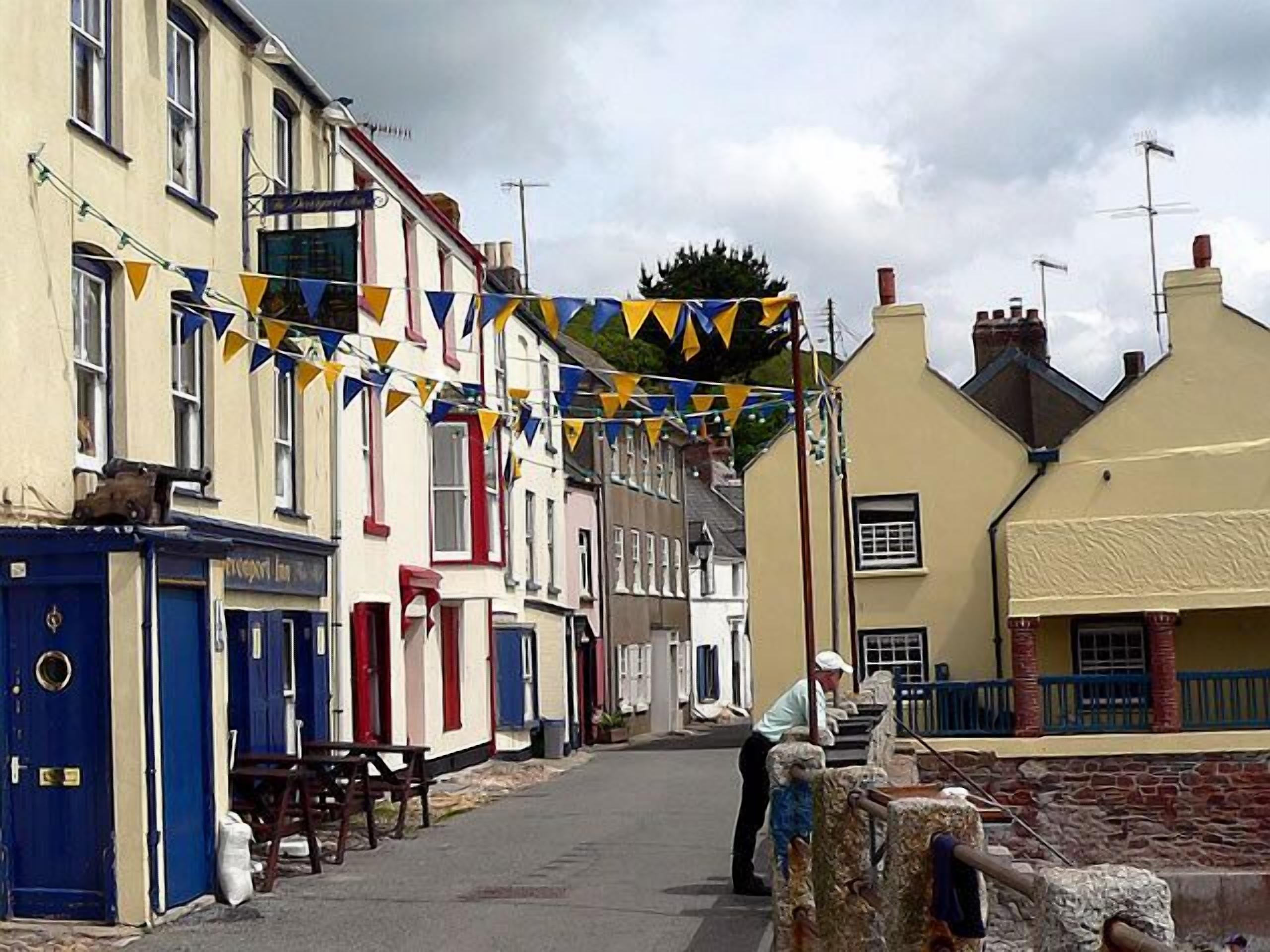 Une rue étroite bordée de bâtiments traditionnels, dont certains ont des portes bleues et d’autres des éléments décoratifs rouges.