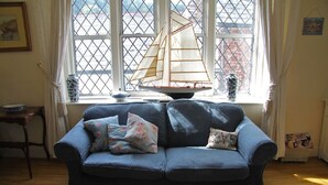 Una habitación con un sofá azul, una maqueta de un velero y una ventana con vista a edificios.
