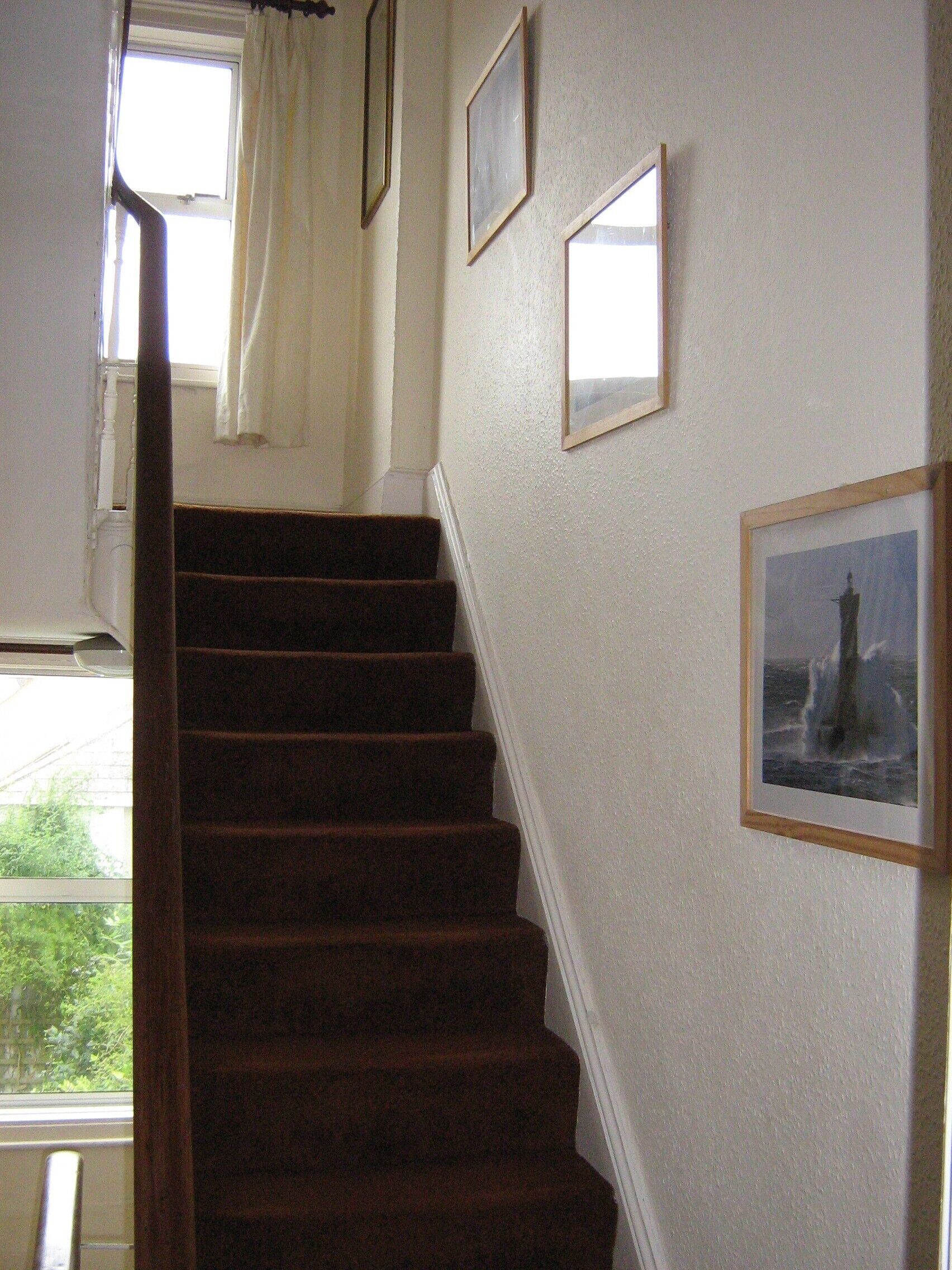 Un escalier avec une rampe, des murs blancs et des tableaux encadrés.