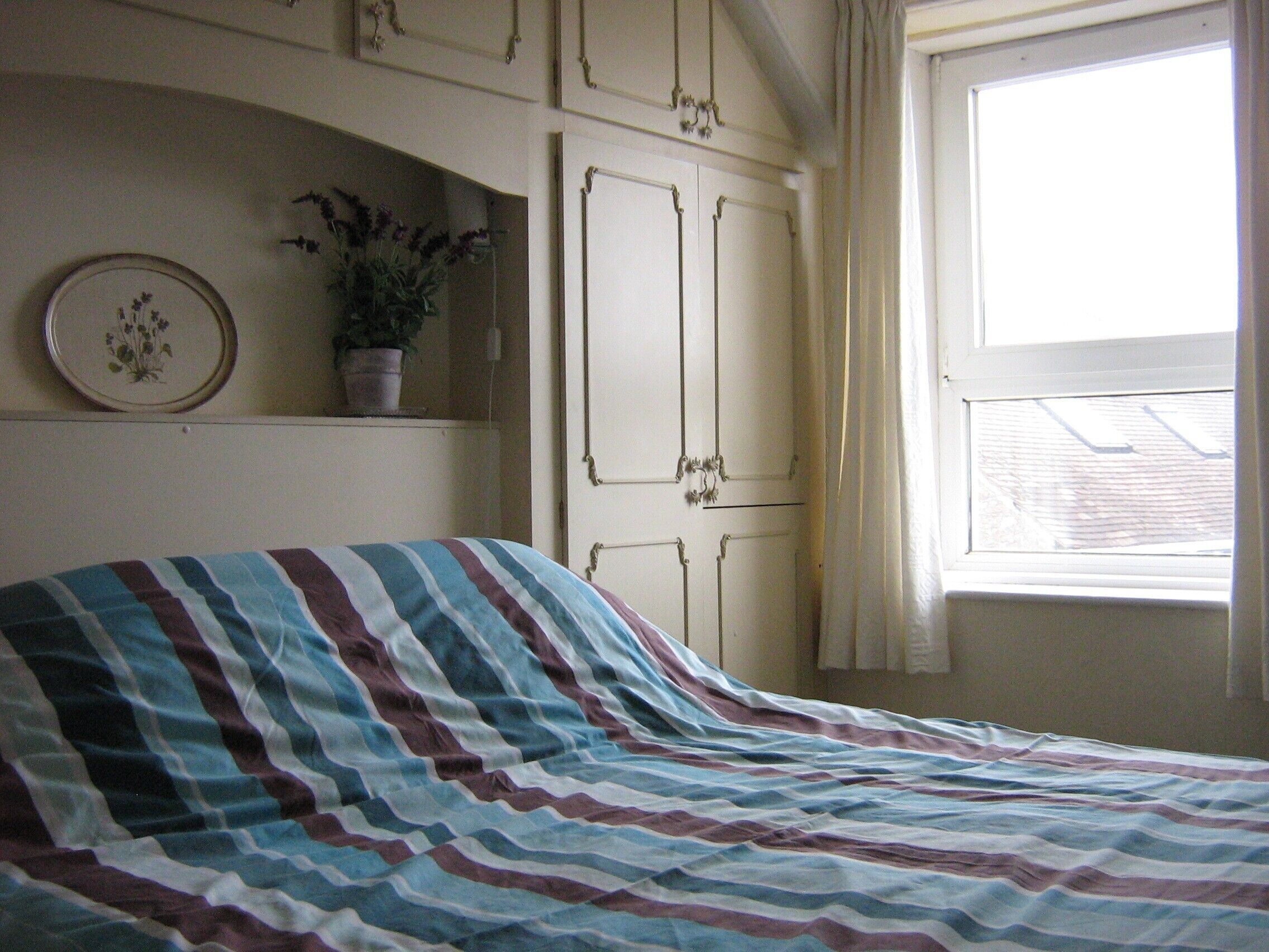 Ein Schlafzimmer mit einem Bett, einer Topfpflanze, einem gerahmten Bild und einem Fenster.