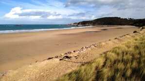 Un'ampia spiaggia sabbiosa con onde calme, dune erbose e una collina lontana con vegetazione.