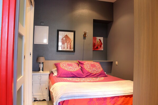 A bedroom with a bed, nightstand, and two wall-mounted light switches. - Beach Studio - Villas des Sables (Fréhel)