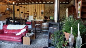 Een rustiek interieur met een rode leren bank, een houten bar, een grote metalen kachel en diverse keukengerei.
