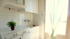 Een keuken met witte betegelde wanden, een fornuis en een spoelbak.
