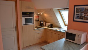 Una cocina con armarios de madera, microondas y ventana con vista al campo.