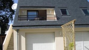 Una casa de dos pisos con techo inclinado, un garaje frontal y un pequeño balcón.
