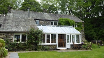 A house with a stone exterior, a glass conservatory, and a well-maintained lawn.