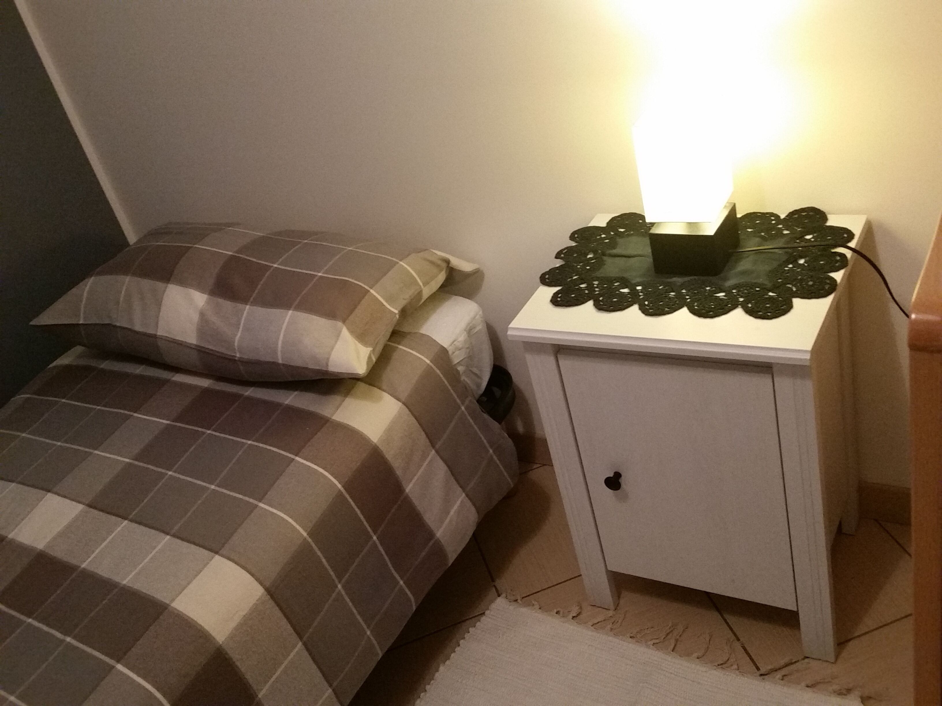 Un dormitorio pequeño con una cama, una mesita de noche con lámpara y un armario.