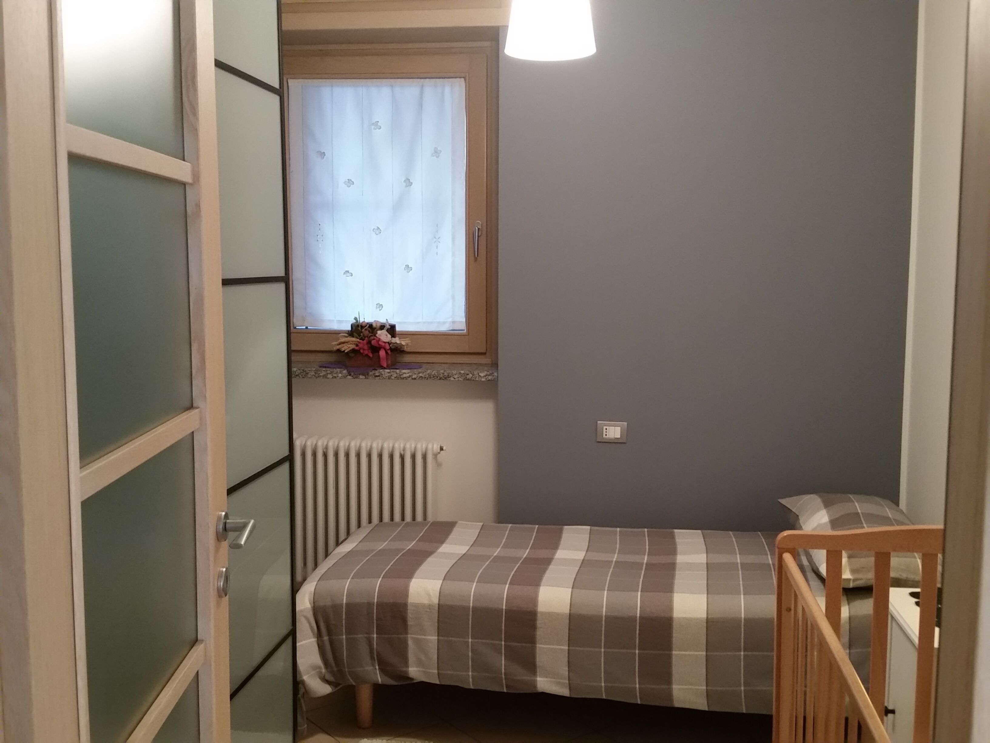 Een kleine slaapkamer met een enkel bed, een raam met gordijn, een radiator en een houten ledikant.