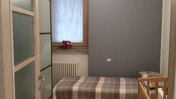 Een kleine slaapkamer met een enkel bed, een raam met gordijn, een radiator en een houten ledikant.