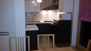 Ett kompakt kök med vita skåp, en svart spis och en mikrovågsugn.