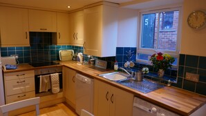 A kitchen with wooden cabinets, a built-in oven, a dishwasher, and a window with a view of a brick building. - THE NOOK, a cosy 3 bed cottage, newly renovated & pet friendly in Tideswell (Tideswell, Derbyshire)