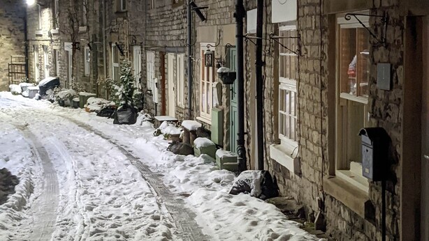 A snow-covered street with stone buildings, a visible tire track, and a street lamp. - THE NOOK, a cosy 3 bed cottage, newly renovated & pet friendly in Tideswell (Tideswell, Derbyshire)