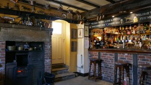 A bar area with a brick fireplace, shelves with copper pots, and a variety of bottles and glasses. - THE NOOK, a cosy 3 bed cottage, newly renovated & pet friendly in Tideswell (Tideswell, Derbyshire)
