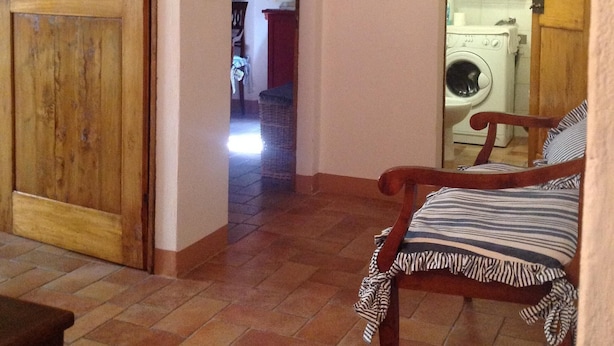 Ein Flur mit einer Holztür, einem Stuhl mit gestreifter Sitzkissen und einer Waschmaschine im Hintergrund.
