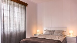 Ein Schlafzimmer mit einem Bett, zwei Nachttischen und einem Fenster mit Vorhängen.
