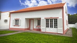 Ein eingeschossiges Gebäude mit rotem Ziegeldach, weißen Wänden und einer kleinen Veranda mit Tisch und Stühlen.