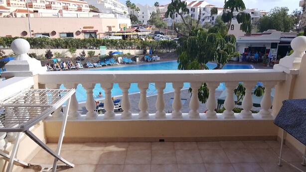 Zona de piscina con sillones, una pequeña mesa y vistas a la piscina y edificios circundantes.
