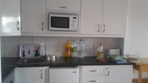 Una cocina con gabinetes blancos, un microondas, un lavabo y varios objetos sobre la encimera.