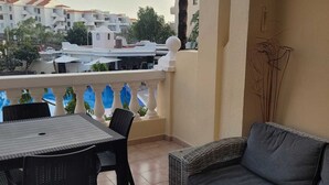 Un balcón con mesa y sillas, un sofá y vistas a edificios y árboles.