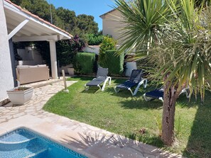 Un patio trasero con piscina, sillas de descanso y un área de patio techada.