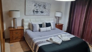 A neatly arranged hotel room with a bed, bedside tables, a lamp, a painting, and a window with curtains.