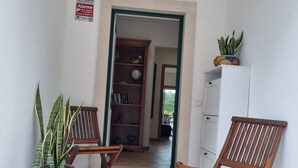 A hallway with two wooden chairs, a potted plant, a bookshelf, and a cabinet.