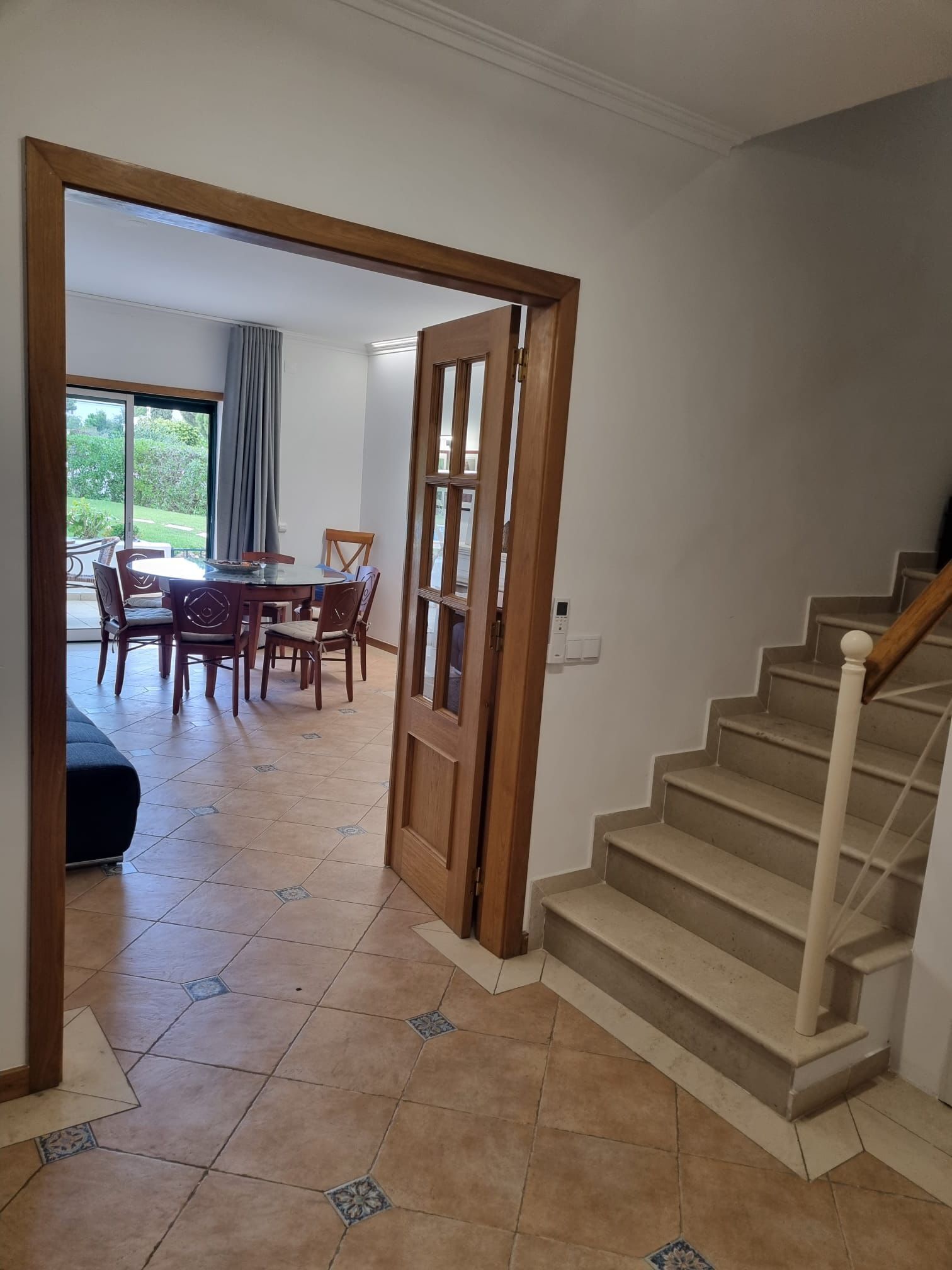 A spacious living area with a dining table and chairs, a staircase, and a view of the outdoors.