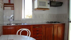 Une cuisine avec une table blanche, des placards en bois, un four à micro-ondes blanc et une fenêtre.