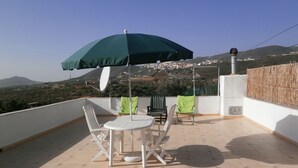 Une terrasse avec une table et des chaises, un parasol vert et une vue sur une ville au loin.