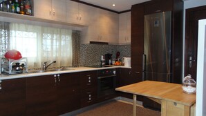A modern kitchen with dark wooden cabinets, a stainless steel refrigerator, and a wooden dining table. - Elegant and cozy apartment (Santorini)