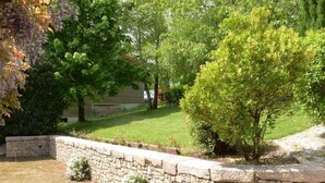 A stone retaining wall with a small garden area, a variety of trees, and a house in the background. - GITE CLOSE TO PUY DU FOU 10 mins FROM VILLA MAGDALENA (Sèvremont)