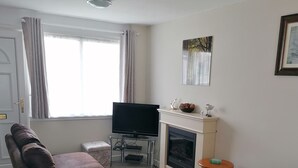 Una sala de estar con un sofá de cuero marrón, un televisor de pantalla plana, una chimenea y una pequeña mesa de madera.